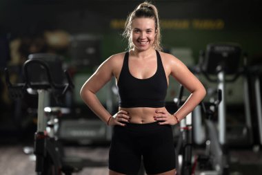 Formda bir kadın, yoğun bir egzersizden sonra spor salonunda kendine güvenen bir poz verir. Gücünü, bağlılığını ve gelişimini gösterir.