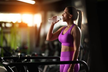 Fit bir kadın koşu bandında koştuktan sonra dinleniyor ve yoğun bir kondisyon egzersizi yapıyor. İyileşmesi ve şarj olması için zaman ayırıyor.