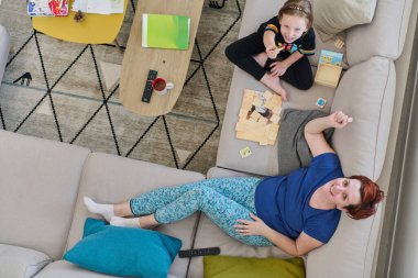 Bir anne ve kızın evdeki koltukta oturup eğlenceli ve büyüleyici bir masa oyunu oynamalarının iç açıcı görüntüsü..