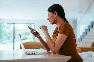 Oturma odasında dizüstü bilgisayar ve akıllı telefon kullanarak oturan bir kadın iş arkadaşları ve akrabalarıyla yaptığı görüntülü konuşmaya bakıyor. İş görüşmesi soruları yanıtlıyor