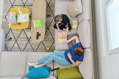 Bir anne ve kızın evdeki koltukta oturup eğlenceli ve büyüleyici bir masa oyunu oynamalarının iç açıcı görüntüsü..