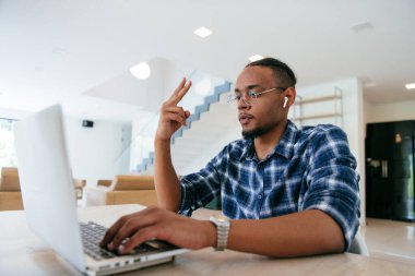 Modern bir oturma odasındaki masada oturan gözlüklü Afrikalı Amerikalı etkileyiciler iş görüşmesi, arkadaşlarla sohbet ve eğlence için dizüstü bilgisayar kullanıyorlar.