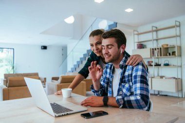 Genç evli bir çift, modern evlerinin oturma odasında otururken bir dizüstü bilgisayarla ebeveynleri, aileleri ve arkadaşlarıyla konuşuyor.
