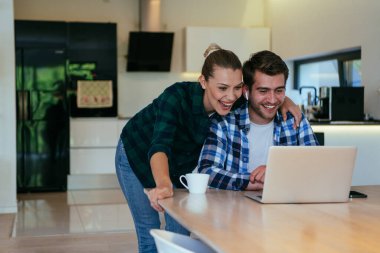 Genç evli bir çift, modern evlerinin oturma odasında otururken bir dizüstü bilgisayarla ebeveynleri, aileleri ve arkadaşlarıyla konuşuyor.