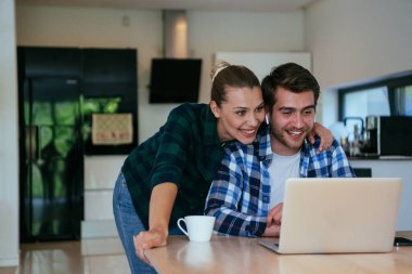 Genç evli bir çift, modern evlerinin oturma odasında otururken bir dizüstü bilgisayarla ebeveynleri, aileleri ve arkadaşlarıyla konuşuyor.