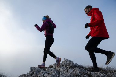 Sabahın erken saatlerinde dağın tepesinde koşan atlet çift patikası. Gökyüzü koşma konsepti, arka planda gökyüzü varken sınırda koşmak tehlikeli. Sağlıklı yaşam, kardiyo egzersizi, spor.