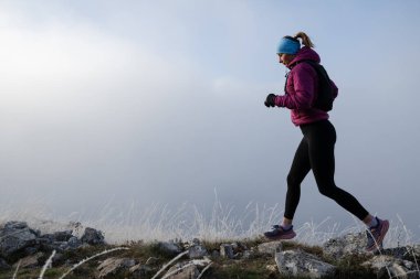 Koşan kadın sporcu, dağdaki ultra-maraton yarışına hazırlanıyor. Açık havada antrenman yapan koşucu bir kadın aktif ve zinde bir hayat sürüyor. Siluet sabahın erken saatlerinde.