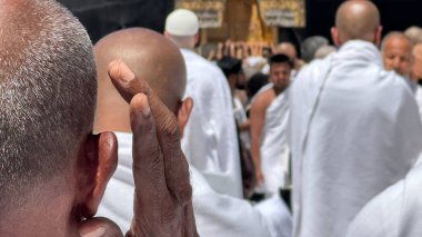 Bir grup Müslüman hacı beyaz hacı kıyafetleri içinde Suudi Arabistan 'ın Mekke kentindeki Kabe yakınlarında hac yapıyorlar. Ruhani bir atmosferi olan, dua ederken elini kaldıran bir adamın yakın çekimi..