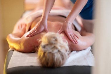 Spa 'da Sırt Masajı. Mavi üniformalı profesyonel bir masaj terapisti masaj masasında yatan bir müşteriye rahatlatıcı bir sırt masajı sağlar.