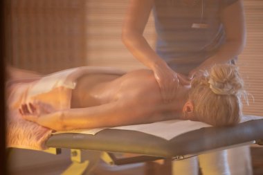 Spa 'da Sırt Masajı. Mavi üniformalı profesyonel bir masaj terapisti masaj masasında yatan bir müşteriye rahatlatıcı bir sırt masajı sağlar.