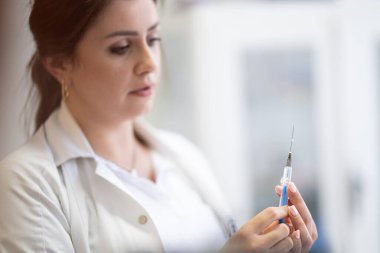 Beyaz önlüklü, odaklanmış bir hemşire profesyonel bir sağlık ortamında enjeksiyon için dikkatlice bir şırınga hazırlar.