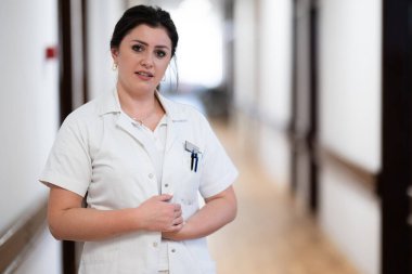 Kendini işine adamış bir hemşire iyi aydınlatılmış bir hastane koridorunda hızla yürüyor. Sağlık hizmetlerindeki profesyonelliği ve aciliyeti yansıtıyor.