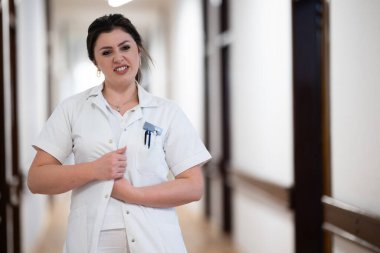 Kendini işine adamış bir hemşire iyi aydınlatılmış bir hastane koridorunda hızla yürüyor. Sağlık hizmetlerindeki profesyonelliği ve aciliyeti yansıtıyor.