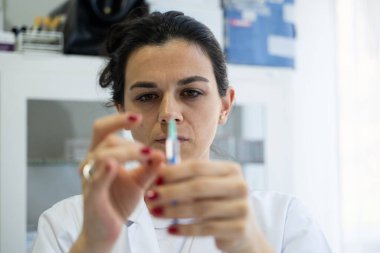 Beyaz önlüklü, odaklanmış bir hemşire profesyonel bir sağlık ortamında enjeksiyon için dikkatlice bir şırınga hazırlar.