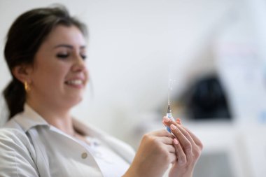 Beyaz önlüklü, odaklanmış bir hemşire profesyonel bir sağlık ortamında enjeksiyon için dikkatlice bir şırınga hazırlar.