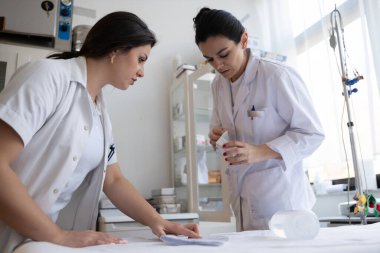 Bir hastane laboratuvarında iki hemşire hastalar ve hastane kullanımı için ilaçları dikkatlice inceliyor ve hazırlıyorlar.