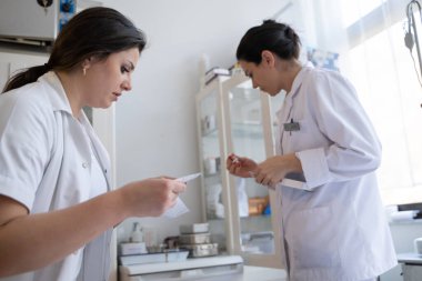 Bir hastane laboratuvarında iki hemşire hastalar ve hastane kullanımı için ilaçları dikkatlice inceliyor ve hazırlıyorlar.