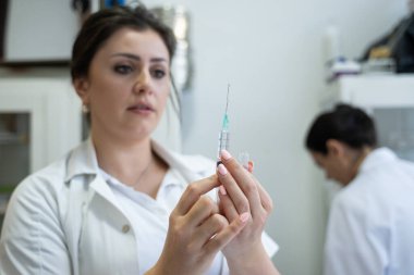 Beyaz önlüklü, odaklanmış bir hemşire profesyonel bir sağlık ortamında enjeksiyon için dikkatlice bir şırınga hazırlar.