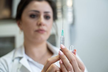 Beyaz önlüklü, odaklanmış bir hemşire profesyonel bir sağlık ortamında enjeksiyon için dikkatlice bir şırınga hazırlar.