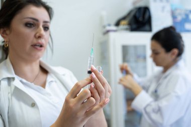 Beyaz önlüklü, odaklanmış bir hemşire profesyonel bir sağlık ortamında enjeksiyon için dikkatlice bir şırınga hazırlar.