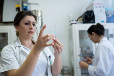 Beyaz önlüklü, odaklanmış bir hemşire profesyonel bir sağlık ortamında enjeksiyon için dikkatlice bir şırınga hazırlar.