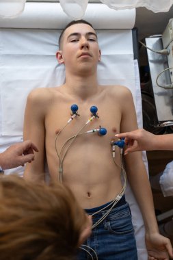 Kadın bir doktor, hastane odasında genç bir adama EKG çeker. Rutin bir kontrol sırasında kalp sağlığını dikkatle izler.