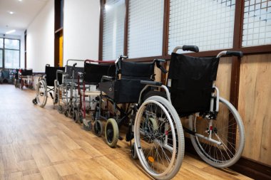 Bir sıra tekerlekli sandalye hastane koridorunda düzgün bir şekilde dizilmiş, hareket desteğine ihtiyacı olan hastalar için.. 