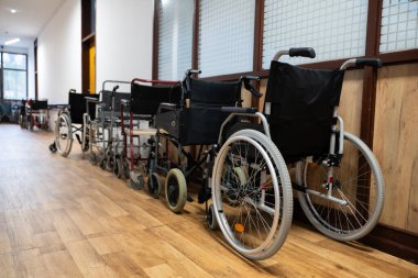 Bir sıra tekerlekli sandalye hastane koridorunda düzgün bir şekilde dizilmiş, hareket desteğine ihtiyacı olan hastalar için.. 
