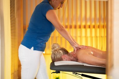 Spa 'da Sırt Masajı. Mavi üniformalı profesyonel bir masaj terapisti masaj masasında yatan bir müşteriye rahatlatıcı bir sırt masajı sağlar.
