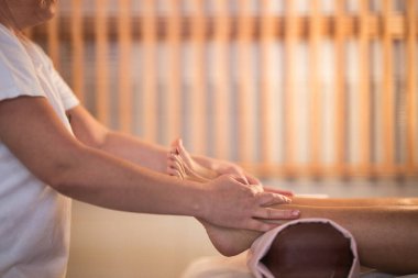 Beyaz üniformalı profesyonel bir masaj terapisti, sakin ve sakin bir spa ortamında müşteriye rahatlatıcı bir ayak masajı sağlar..