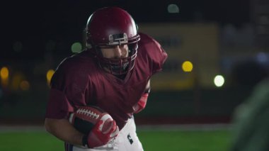 Sahada top atma ve yakalama pratiği yapan Amerikalı bir futbolcu, üniforma ve kask giyerek, dinamik hareketler ve kararlı bir atletik duruş ile becerilerini geliştirmeye odaklandı.