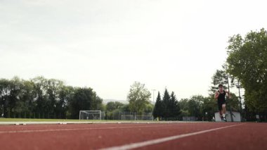 Güneşli bir sabahta atletizm pistinde koşan genç bir sporcunun dikey videosu. Spor anlayışı ve azim. Yüksek kalite 4k görüntü