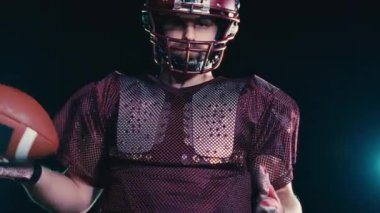 Sahada top atma ve yakalama pratiği yapan Amerikalı bir futbolcu, üniforma ve kask giyerek, dinamik hareketler ve kararlı bir atletik duruş ile becerilerini geliştirmeye odaklandı.