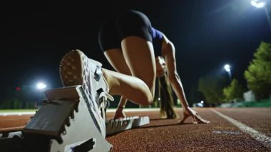 Atletizm atletizm sprint yarışı koşucusu koyu bir arka planda, stadyumun pistinde spor ayakkabılarla koşu koşusuna çıkıyor. Yavaş çekim