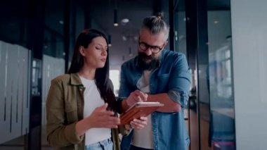 Üst düzey bir hipster akıl hocası ve Avrupalı bir lider, modern bir çalışma alanında tablet üzerinde çalışırken, arka planda yoğun meslektaşlar çalışırken güvenli bir şekilde işbirliği yaparak bir projeyi tartışıyorlar.