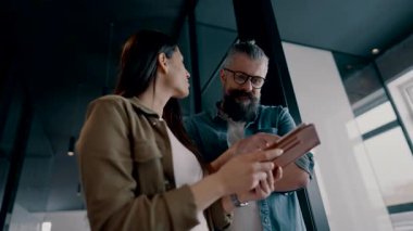 Üst düzey bir hipster akıl hocası ve Avrupalı bir lider, modern bir çalışma alanında tablet üzerinde çalışırken, arka planda yoğun meslektaşlar çalışırken güvenli bir şekilde işbirliği yaparak bir projeyi tartışıyorlar.