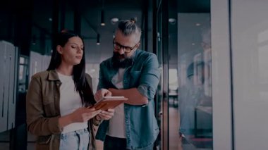 Üst düzey bir hipster akıl hocası ve Avrupalı bir lider, modern bir çalışma alanında tablet üzerinde çalışırken, arka planda yoğun meslektaşlar çalışırken güvenli bir şekilde işbirliği yaparak bir projeyi tartışıyorlar.