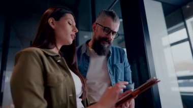 Üst düzey bir hipster akıl hocası ve Avrupalı bir lider, modern bir çalışma alanında tablet üzerinde çalışırken, arka planda yoğun meslektaşlar çalışırken güvenli bir şekilde işbirliği yaparak bir projeyi tartışıyorlar.