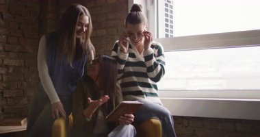 Kadın iş adamları pencere kenarında iş birliği yapıyor, fikirleri tartışıyor ve tablet üzerinde beyin fırtınası yapıyorlar. Modern bir ofiste işbirliği, yaratıcılık ve takım çalışması kavramı