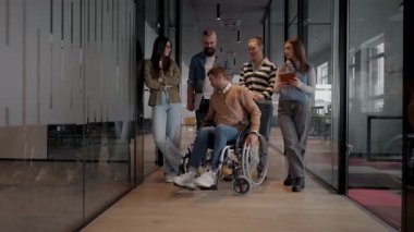 Tekerlekli sandalyede engelli bir iş adamı, modern bir ofiste takım çalışmasının, dahil olmanın ve güçlenmenin gücünü ortaya koyan destekleyici meslektaşlarıyla çevrilidir.. 