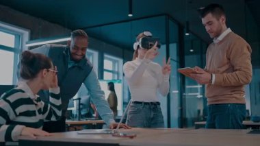 Modern bir iş yerinde çalışan tekerlekli sandalyedeki engelli bir iş kadını. Çevredeki ekip sanal gerçeklik gözlükleri kullanıyor, açık alan yaratıcılığında en son teknolojiyle işbirliği yapıyorlar.