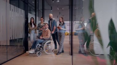 Tekerlekli sandalyede engelli bir iş adamı, modern bir ofiste takım çalışmasının, dahil olmanın ve güçlenmenin gücünü ortaya koyan destekleyici meslektaşlarıyla çevrilidir.. 