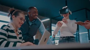 Modern bir iş yerinde çalışan tekerlekli sandalyedeki engelli bir iş kadını. Çevredeki ekip sanal gerçeklik gözlükleri kullanıyor, açık alan yaratıcılığında en son teknolojiyle işbirliği yapıyorlar.