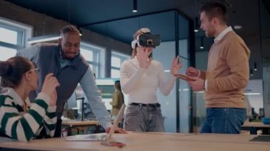 Modern bir iş yerinde çalışan tekerlekli sandalyedeki engelli bir iş kadını. Çevredeki ekip sanal gerçeklik gözlükleri kullanıyor, açık alan yaratıcılığında en son teknolojiyle işbirliği yapıyorlar.