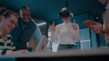 Modern bir iş yerinde çalışan tekerlekli sandalyedeki engelli bir iş kadını. Çevredeki ekip sanal gerçeklik gözlükleri kullanıyor, açık alan yaratıcılığında en son teknolojiyle işbirliği yapıyorlar.