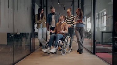 Tekerlekli sandalyede engelli bir iş adamı, modern bir ofiste takım çalışmasının, dahil olmanın ve güçlenmenin gücünü ortaya koyan destekleyici meslektaşlarıyla çevrilidir.. 