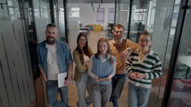 Modern bir ortak çalışma ofisindeki çeşitli profesyonellerden oluşan bir ekip, birlikte gülümsüyor, takım çalışması, işbirliği ve yenilikleri destekleyen pozitif bir şirket kültürü ve dinamik bir çalışma sergiliyor.