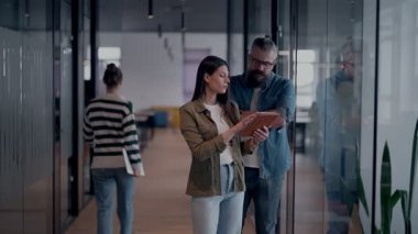 Üst düzey bir hipster akıl hocası ve Avrupalı bir lider, modern bir çalışma alanında tablet üzerinde çalışırken, arka planda yoğun meslektaşlar çalışırken güvenli bir şekilde işbirliği yaparak bir projeyi tartışıyorlar.