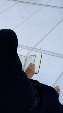Kâbe yakınlarındaki Mescid-i Haram 'da, Umrah veya Hac' ta, Müslüman bir kadın, Kur 'an okur. Mübarek Ramazan Bayramı, inanç ve bağlılık. Huzurlu İslami