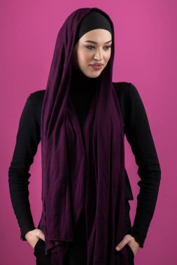 Başörtülü çarpıcı bir Müslüman kadın zarif bir şekilde stüdyoda pembe bir arka plana karşı poz veriyor, zarafet ve güven yayıyor.. 